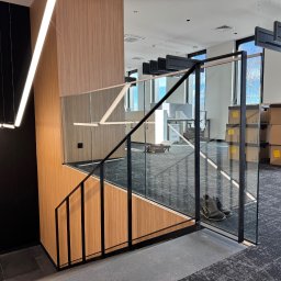 STAL KRAFT - Nowoczesne schody z balustradą szklaną i czarnymi elementami metalowymi w jasnym biurze. Widoczne kartony i oświetlenie sufitowe.