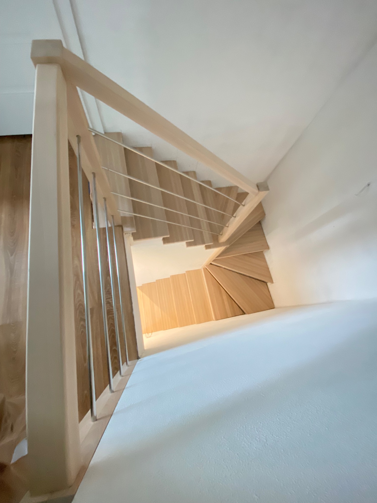 Kątowe ujęcie schodów drewnianych z balustradą ze stalowych prętów, widok z góry na zakręt schodów i białe ściany.