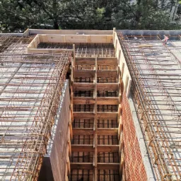 Zbrojenie pod fundament z deskowaniem, widok z góry na siatkę stalową i drewniane szalunki, zieleń drzew w tle.