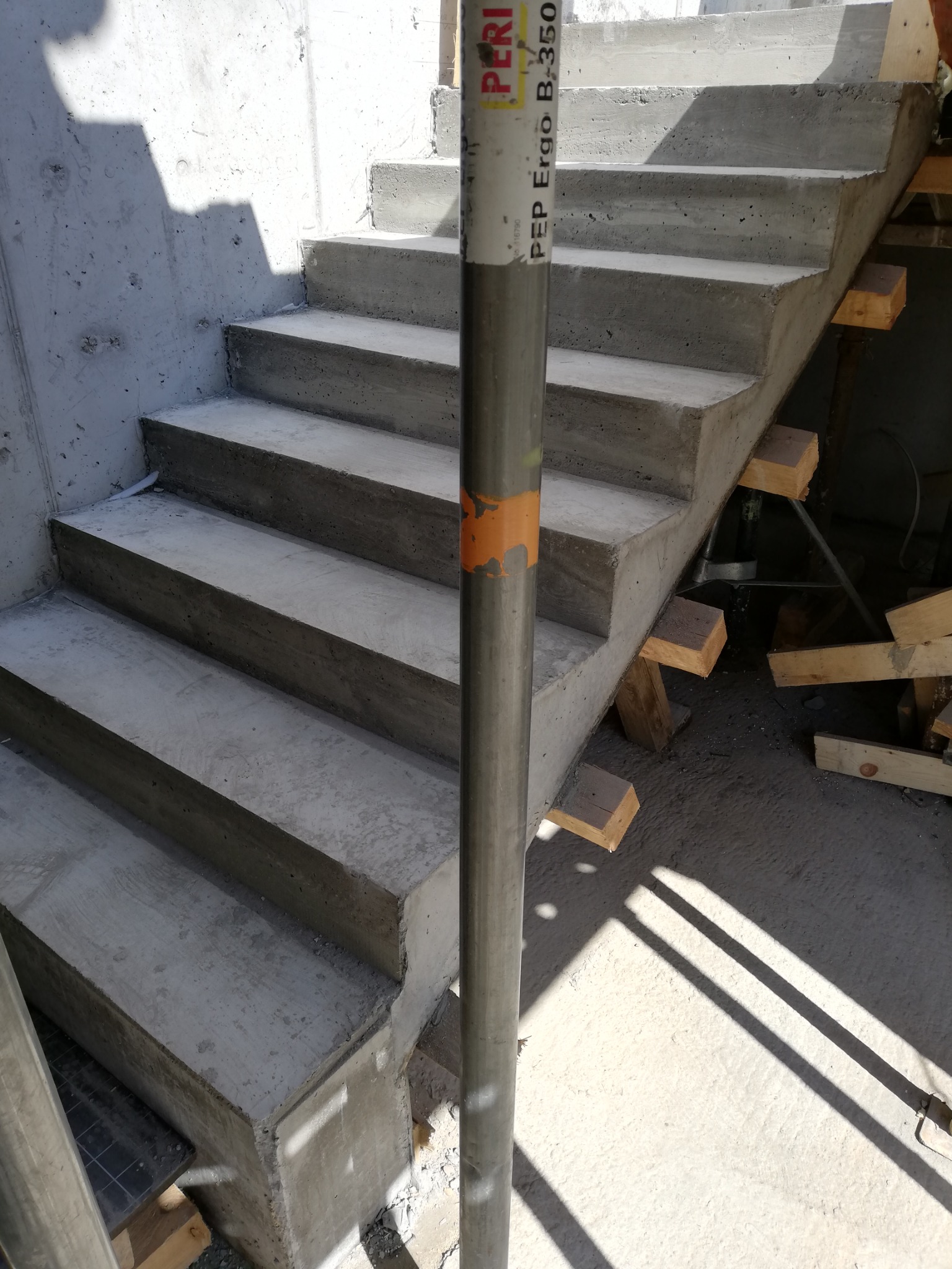 Surowe betonowe schody w trakcie budowy, wsparte na drewnianych podporach, z widocznymi śladami szalunku i metalowym stemplem PERI Ergo B-350.