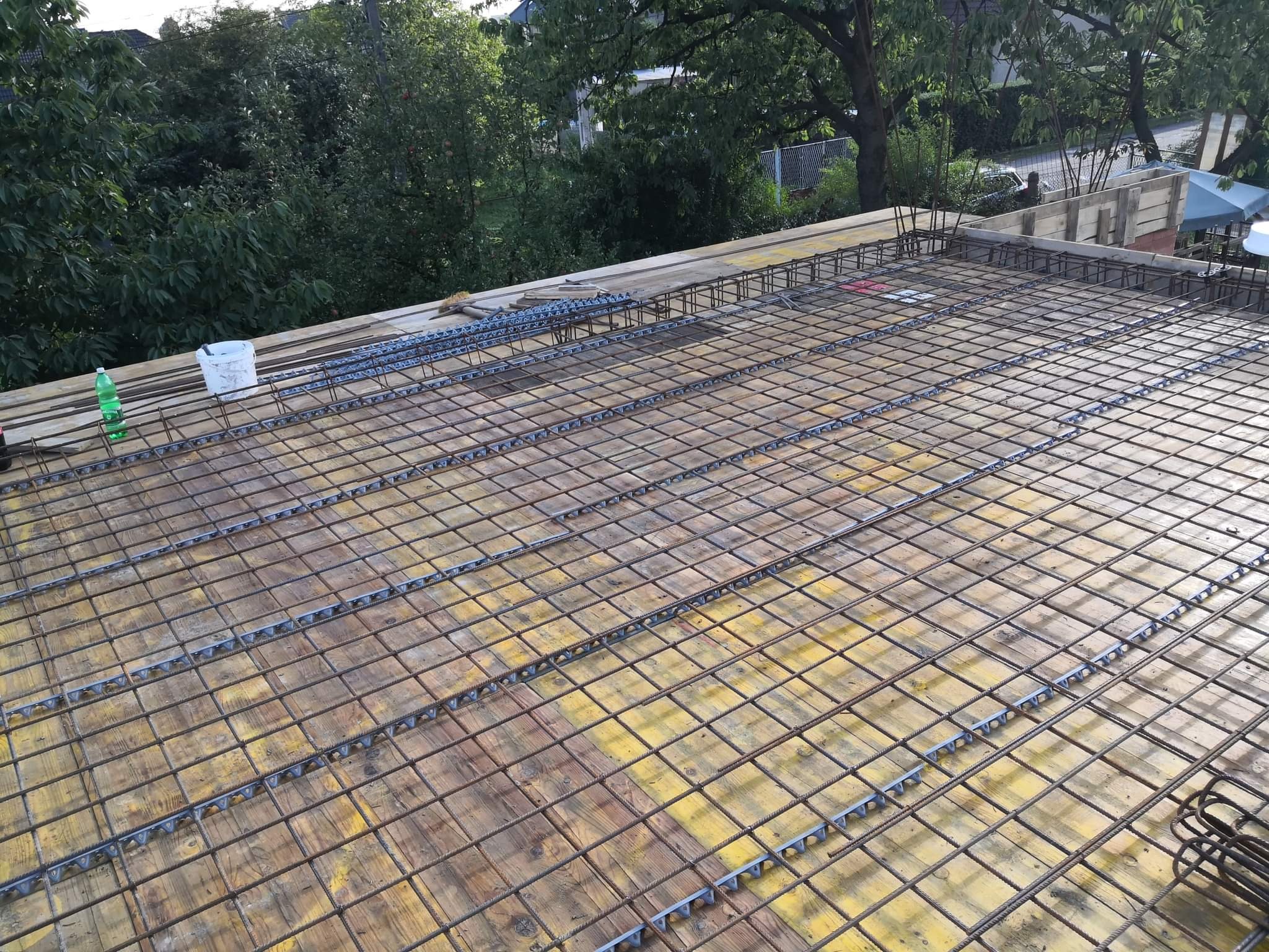 Zbrojenie stropu z siatki stalowej i dystansami z tworzywa na żółtym szalunku, widok z góry na tle zieleni.