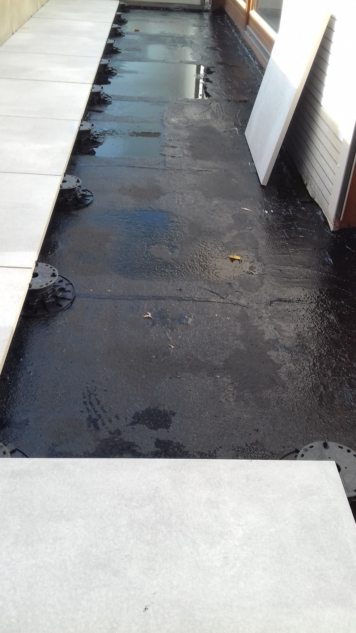 Montaż podłogi na regulowanych wspornikach tarasowych, widoczna hydroizolacja, częściowo ułożone płyty tarasowe w kolorze jasnego beżu.