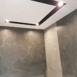 Wykończona łazienka w Skierniewicach z szarymi płytkami imitującymi kamień na ścianach i sufitem z czarnymi, geometrycznymi wstawkami oraz wbudowanym oświetleniem.