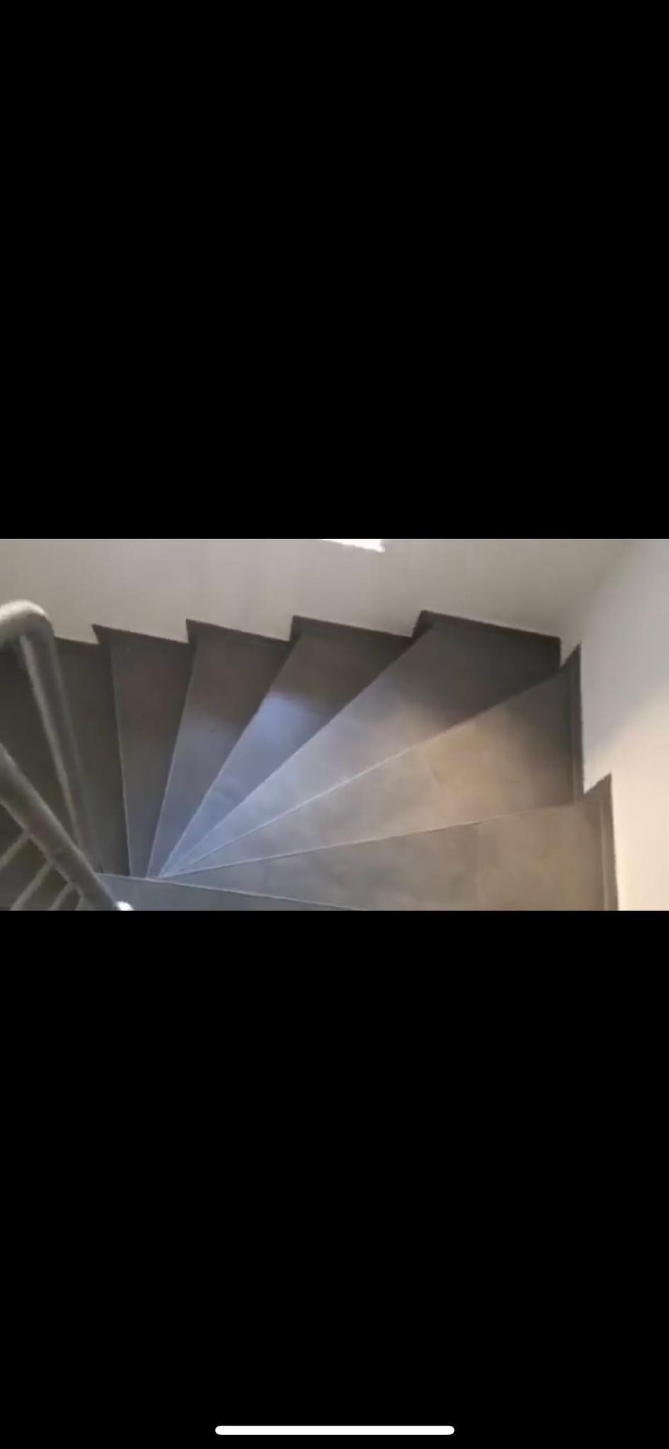 Spiralne schody wyłożone szarymi płytkami, widok z góry, z fragmentem metalowej poręczy.