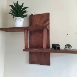 Drewniana półka ścienna o asymetrycznym kształcie, na której stoją doniczka z zieloną rośliną, figurka słonia i pamiątka z Włoch, obok wisi łapacz snów