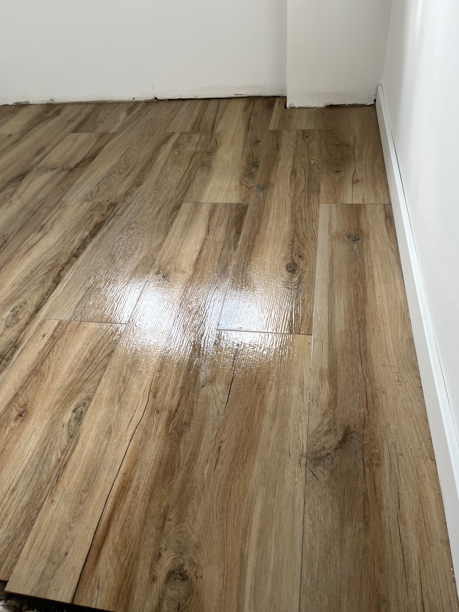 Ułożona podłoga z paneli imitujących drewno, widoczna fuga przy ścianie i niedokończone wykończenie przy listwie przypodłogowej.