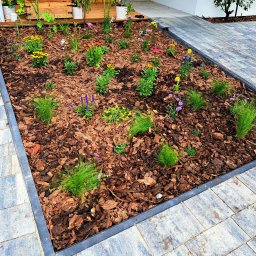 ANMAR Anna Zandecka - Nowo założony rabat kwiatowy z korą, obrzeżem z kostki brukowej i różnorodnymi nasadzeniami: trawy ozdobne, rudbekie, szałwie i inne kwiaty. Widok z góry na ogród przy domu.