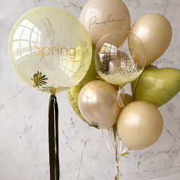 Fundacji Rozwoju Przedsiębiorczości Twój StartUp - Kompozycja z beżowych, zielonych i przezroczystych balonów z napisami 'Spring' i 'Расцветай', wypełnionych konfetti i gałązkami mimozy, na tle marmurowej ściany.