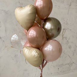 Fundacji Rozwoju Przedsiębiorczości Twój StartUp - Bukiet balonów w odcieniach różu, beżu i złota, z balonem w kształcie serca i przezroczystym balonem z brokatem, zawiązany różową wstążką, na tle marmurowej ściany.