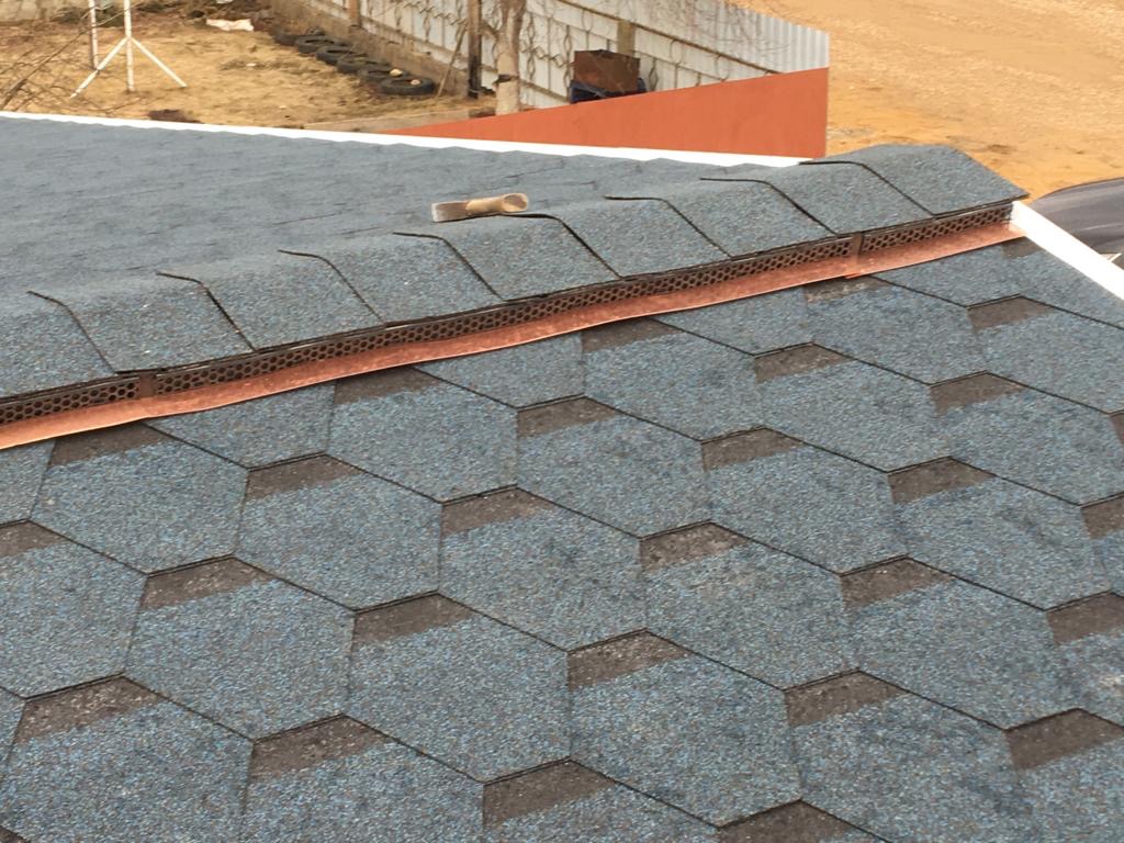 Nowy dach pokryty gontem bitumicznym w odcieniach szarości i niebieskiego, z widoczną miedzianą listwą okapową i elementami wentylacyjnymi przy krawędzi dachu.