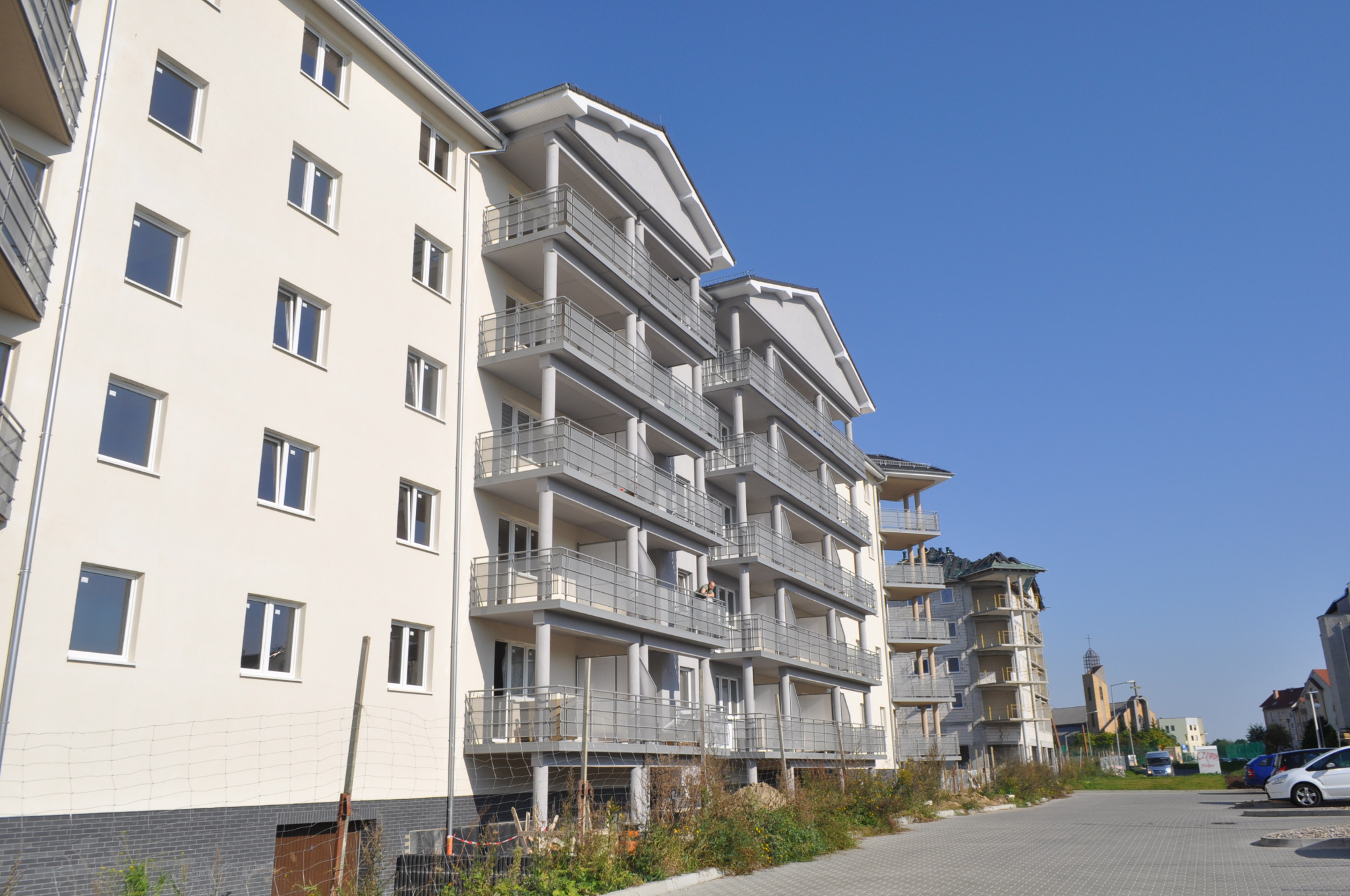 Nowoczesny budynek wielorodzinny z balkonami w Gorzowie Wielkopolskim, widoczny z perspektywy ulicy, z jasną elewacją i szarymi balustradami balkonów.