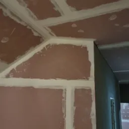 Sufit i ściana z płyt karton-gips, łączenia zaszpachlowane, widoczne nierówności i niedoskonałości szpachlowania, przygotowanie do dalszych prac wykończeniowych.