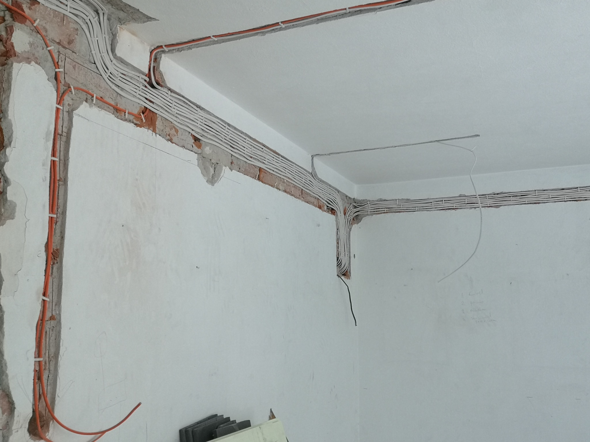 Instalacja elektryczna w trakcie wykonywania w Wołczkowie: widoczne kable prowadzone w bruzdach w ścianie i pod sufitem, zabezpieczone uchwytami, ściany w stanie surowym, przygotowane do dalszych...