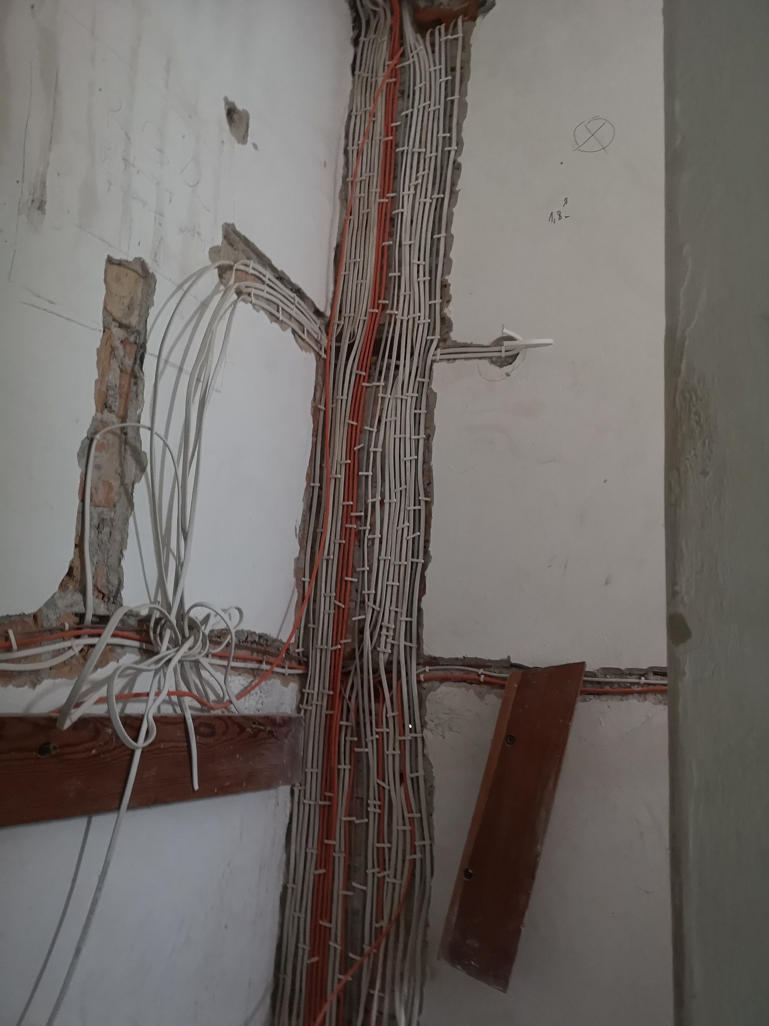 Ściana w trakcie remontu z widocznymi przewodami elektrycznymi w korytkach i luźno wiszącymi, częściowo zamurowanymi w ścianie.
