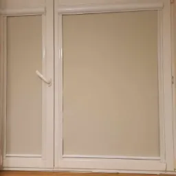 Zamknięte, kremowe rolety w kasecie na białych, plastikowych oknach, widok od wewnątrz.