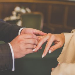 Szymon Korta Fotografia - Moment zakładania obrączki podczas ceremonii ślubnej. Dłonie pary w zbliżeniu, delikatne światło, elegancki garnitur i suknia. Romantyczna atmosfera.