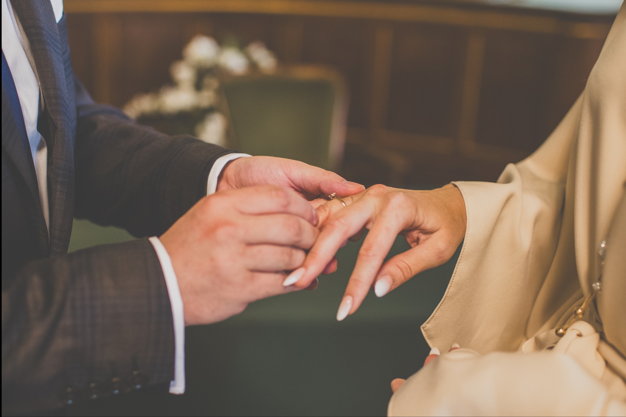 Moment zakładania obrączki podczas ceremonii ślubnej. Dłonie pary w zbliżeniu, delikatne światło, elegancki garnitur i suknia. Romantyczna atmosfera.