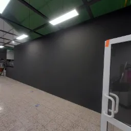 Świeżo pomalowana, matowa, czarna ściana w pomieszczeniu z terakotową podłogą i białymi drzwiami z taśmą zabezpieczającą na framudze.