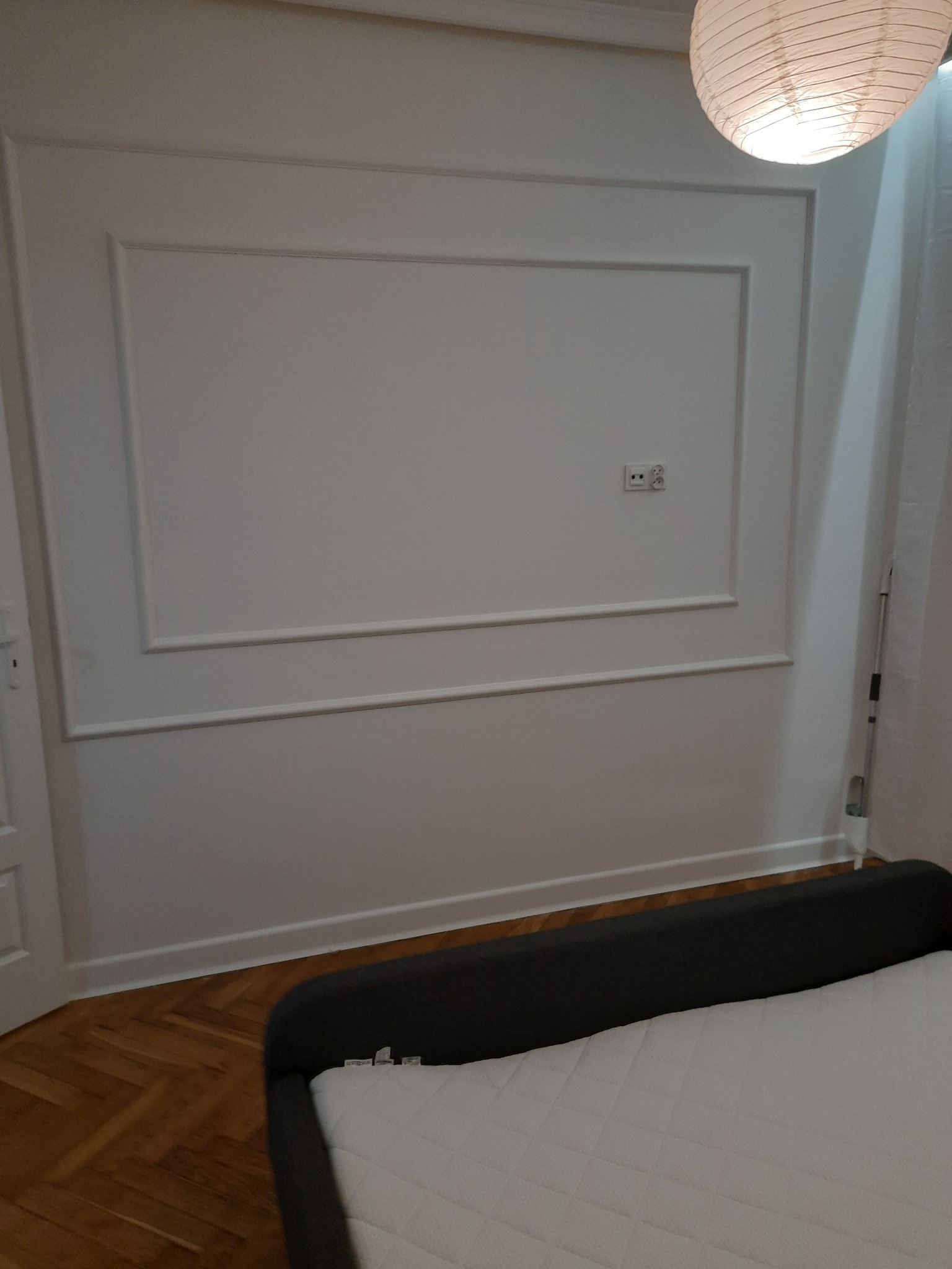Ściana w pokoju po remoncie z dekoracyjnymi listwami i gładzią, widoczny fragment łóżka i lampy w stylu japońskim.