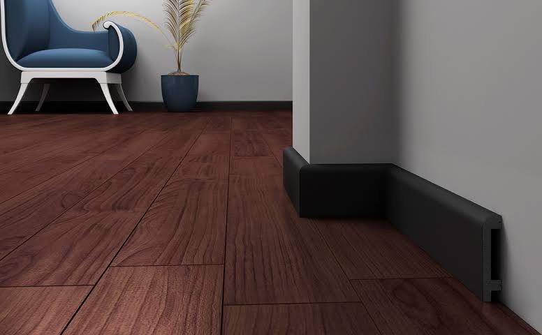 Ciemne, drewniane panele podłogowe z czarnymi listwami przypodłogowymi, uzupełnione krzesłem i rośliną w tle.