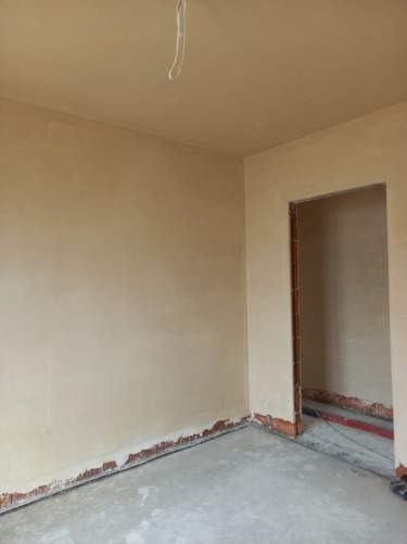 Pokój po nałożeniu wstępnej warstwy gładzi, widoczne niedoskonałości przy podłodze i wystający przewód z sufitu.