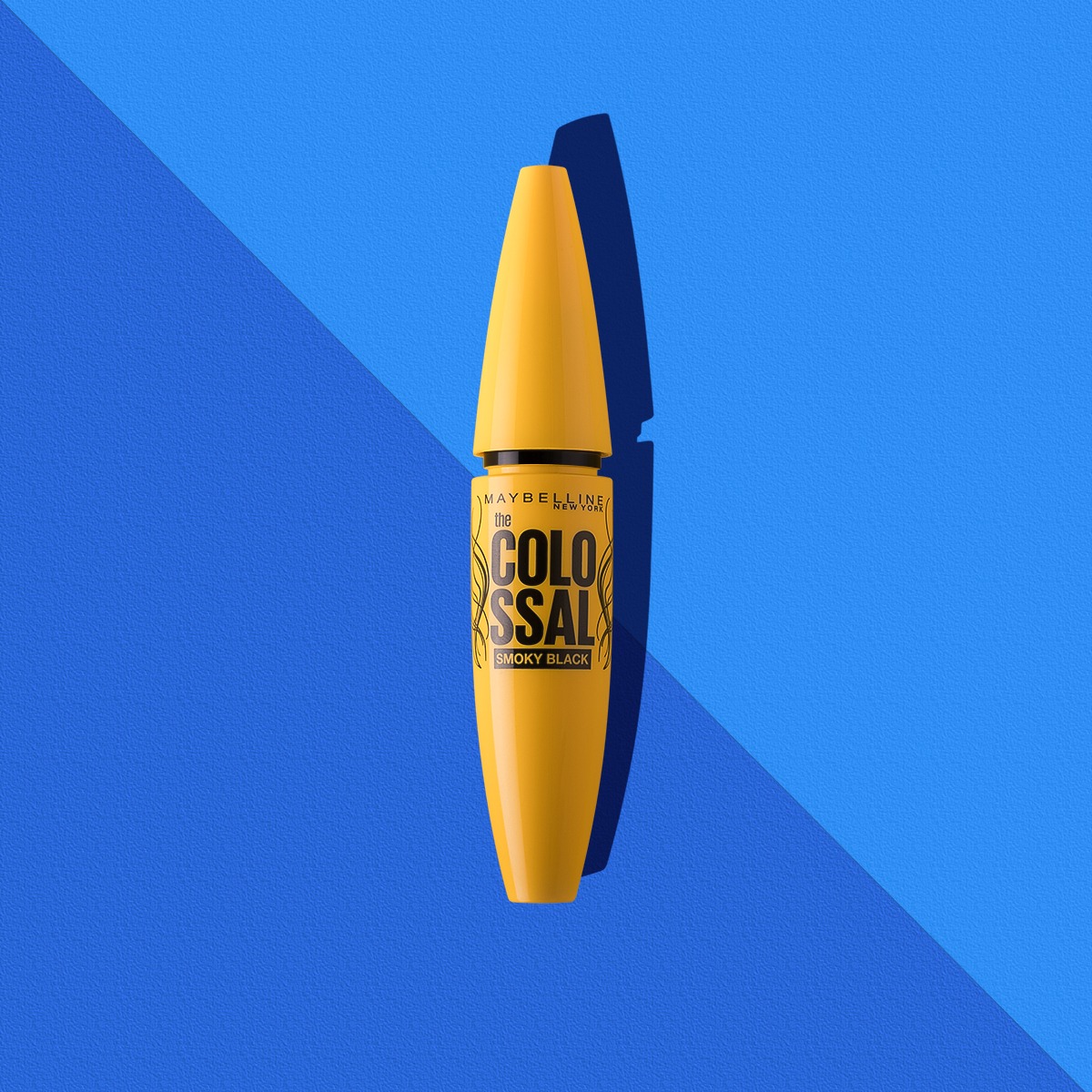 Żółty tusz do rzęs Maybelline Colossal Smoky Black na niebieskim tle z cieniem.