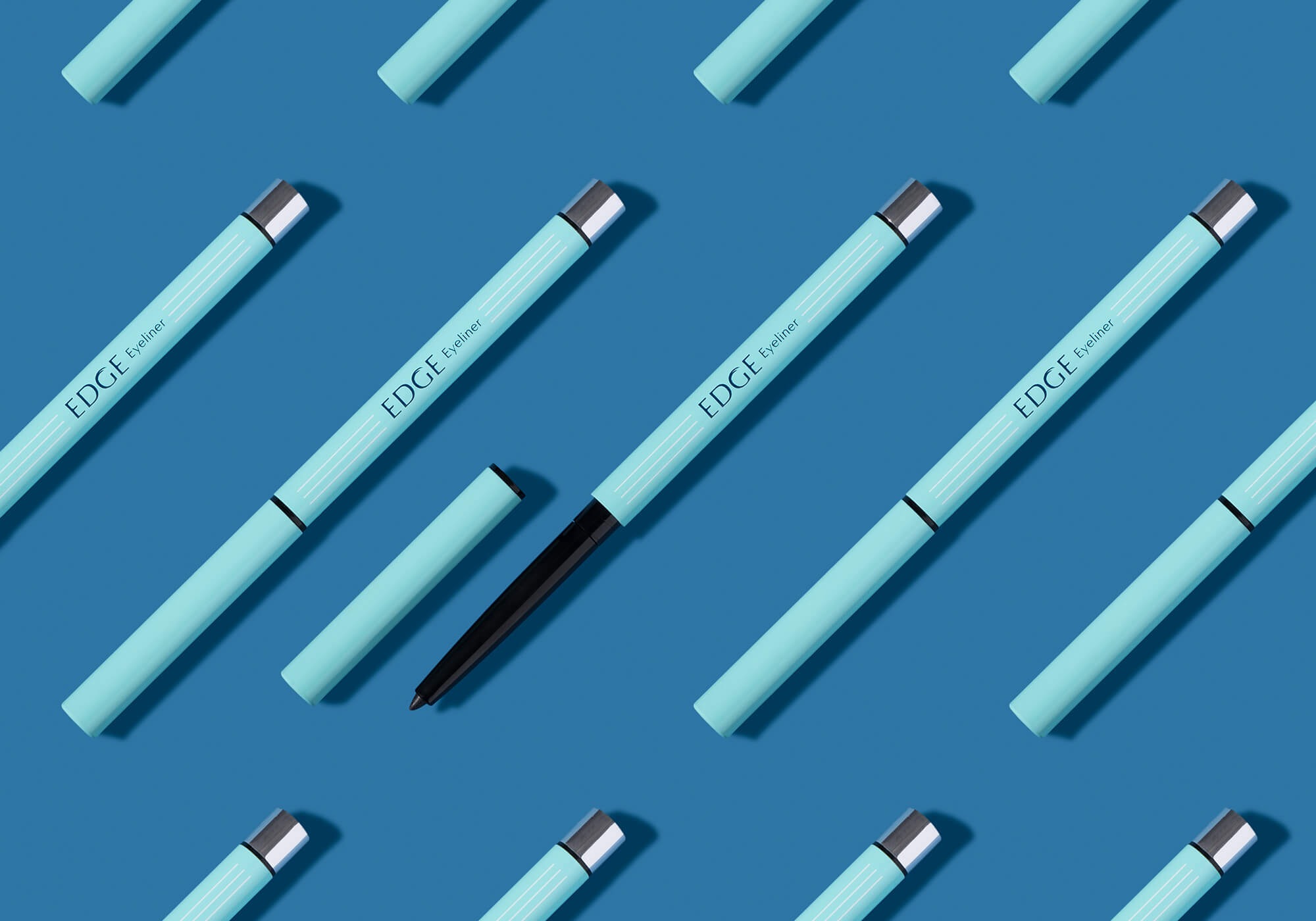 Turkusowe kredki do oczu Edge Eyeliner ułożone równolegle na niebieskim tle, jedna z otwartą nasadką i wysuniętym czarnym wkładem.