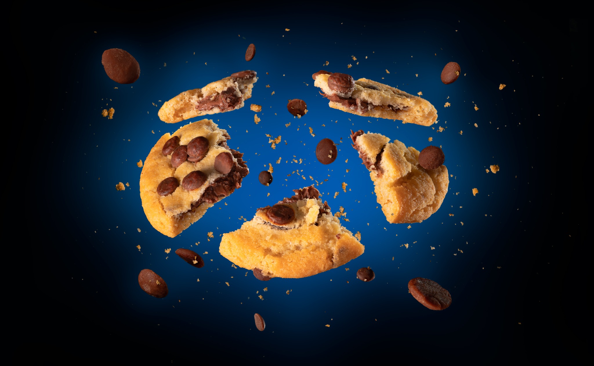 Rozpadający się na kawałki ciasteczko z kawałkami czekolady na niebieskim tle, z widoczną strukturą i okruchami.