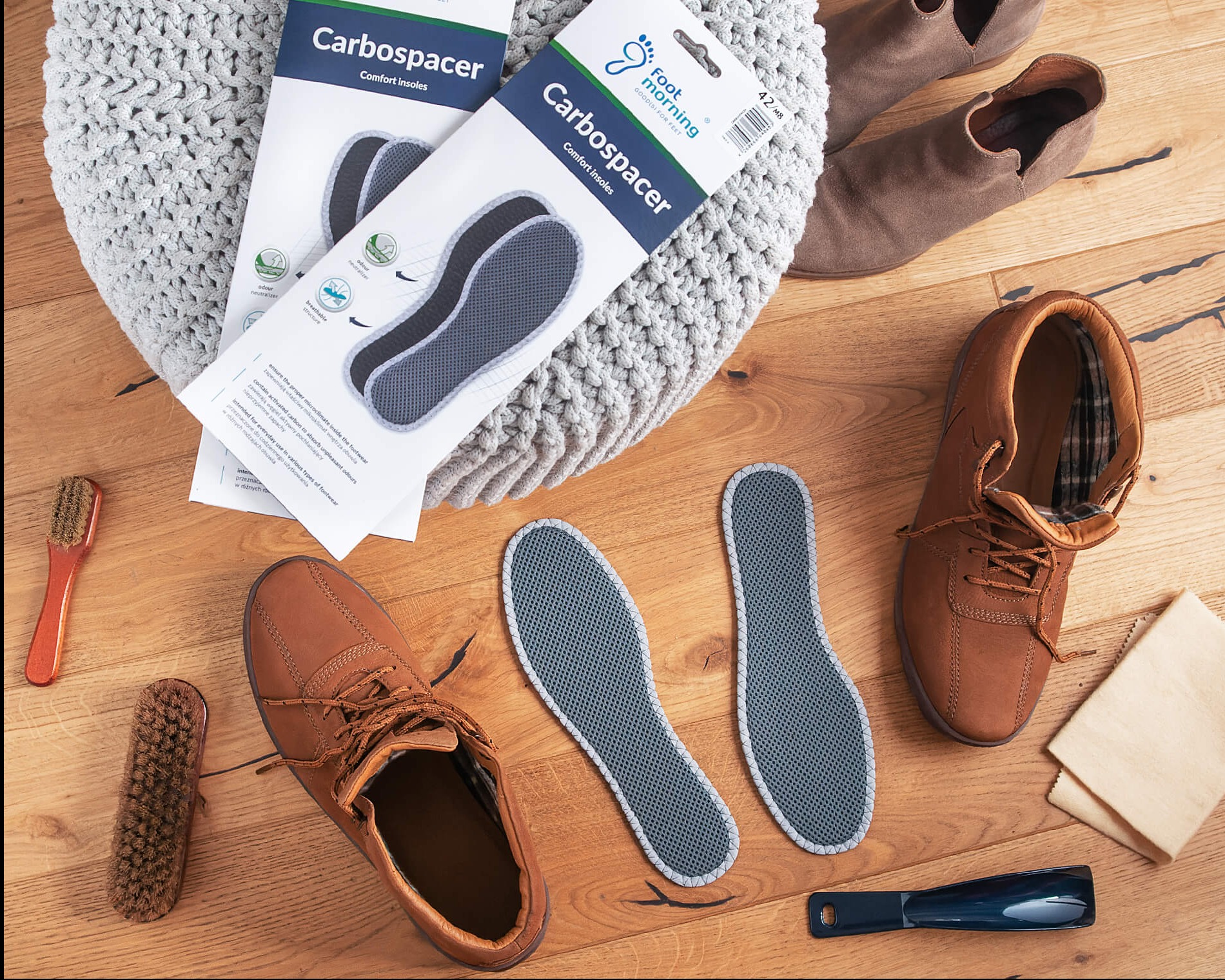 Para wkładek do butów Carbospacer obok brązowych butów, szczotek do czyszczenia i łyżki do butów, ułożonych na drewnianej podłodze.