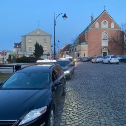 Taxi Rzeszów - Rząd czarnych taksówek typu kombi ustawionych na brukowanej ulicy w Rzeszowie, z budynkiem kościoła i kamienicą w tle, wczesnym rankiem.
