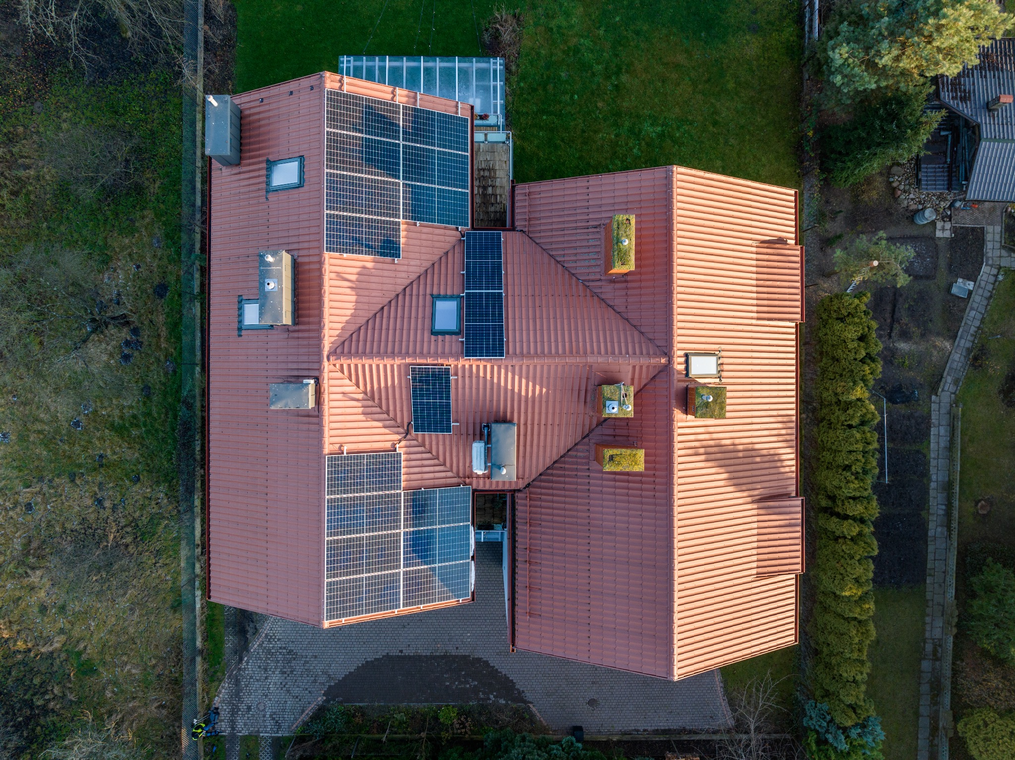 Widok z drona na dach domu z panelami fotowoltaicznymi, z kominem porośniętym mchem, w otoczeniu zieleni.