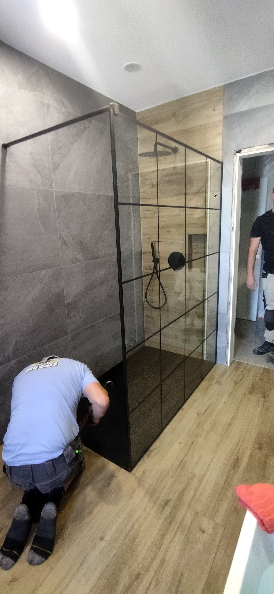 Montaż kabiny prysznicowej typu walk-in z czarnymi profilami w łazience w Lesznie, widoczny instalator w trakcie pracy.