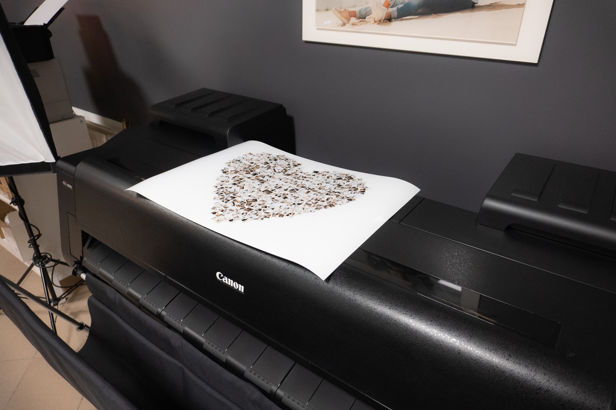 Wydruk w kształcie serca, utworzony z kolażu małych fotografii, leżący na drukarce Canon w studiu fotograficznym z widocznym oświetleniem studyjnym.