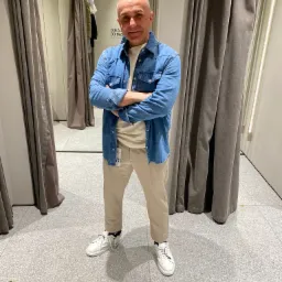 Mężczyzna w przymierzalni w Krakowie prezentuje casualowy zestaw: dżinsowa koszula, beżowe spodnie i białe sneakersy.