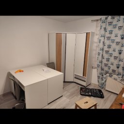 Remontowo - Montaż narożnej szafy z lustrem w pokoju, widoczny rozłożony zestaw narzędzi i taboret, zasłony w sowy.