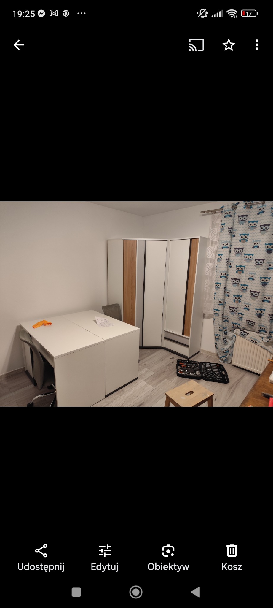 Montaż narożnej szafy z lustrem w pokoju, widoczny rozłożony zestaw narzędzi i taboret, zasłony w sowy.