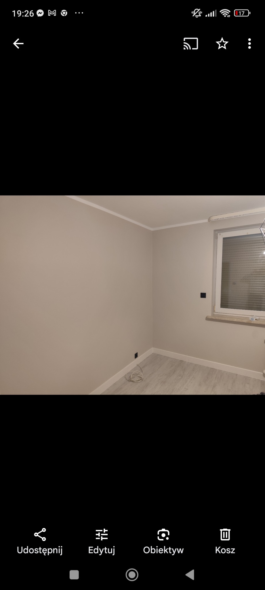 Pomalowane na beżowo ściany pokoju z szarą podłogą, białą listwą przypodłogową i sufitową oraz oknem z białymi żaluzjami.