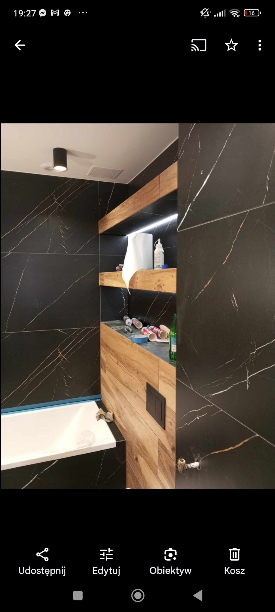 Częściowo wykończona łazienka w Nowym Sączu z czarnymi płytkami imitującymi marmur, drewnianymi elementami zabudowy, białą wanną i widocznymi materiałami budowlanymi sugerującymi trwający remont.