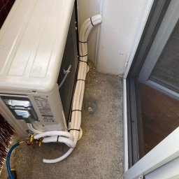 SYSCON - Zewnętrzna jednostka klimatyzacji Toshiba zamontowana na balkonie, z widocznymi przewodami zabezpieczonymi czarnymi opaskami i podłączonymi narzędziami serwisowymi.