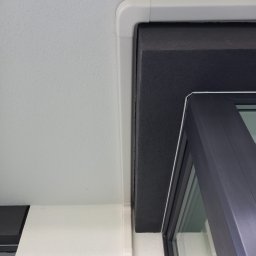 SYSCON - Szczegół izolacji termicznej wokół okna z widoczną białą listwą maskującą i czarną pianką izolacyjną.