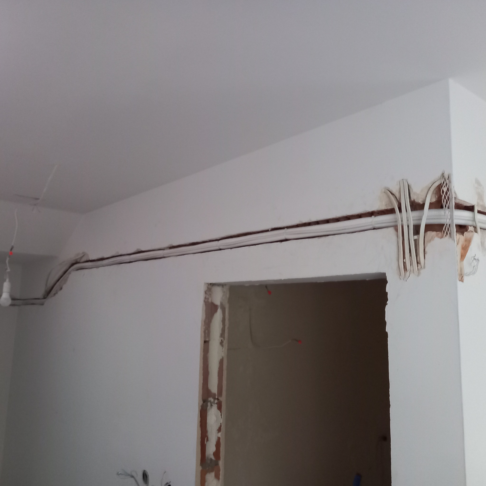 Instalacja przewodów wentylacyjnych w nowym budynku, widoczne prowadzone przewody w ścianie i suficie, etap prac wykończeniowych.