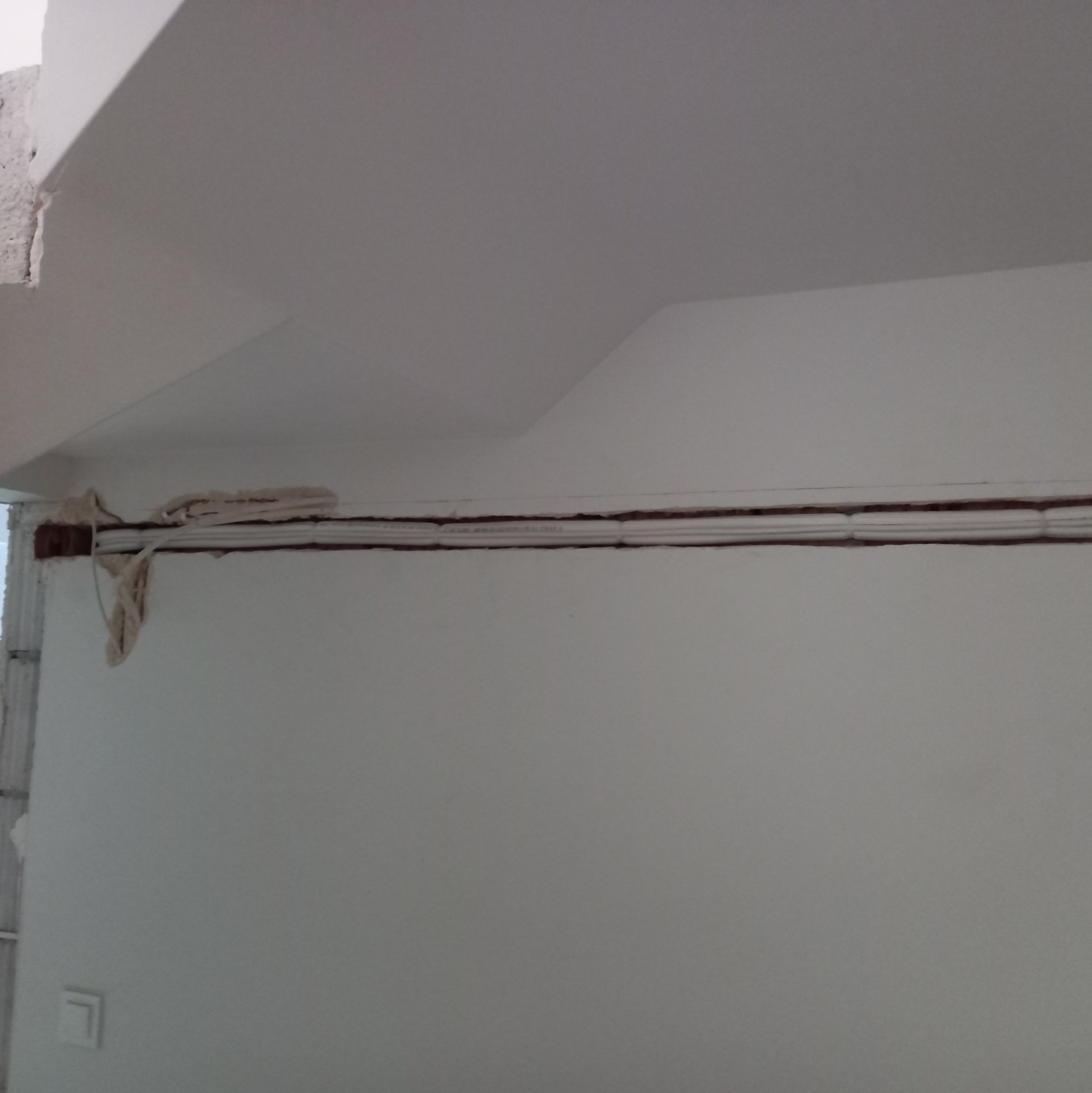 Biała ściana z widocznymi przewodami w listwie i zabezpieczeniem z szmaty na rogu, przygotowana do prac wykończeniowych.