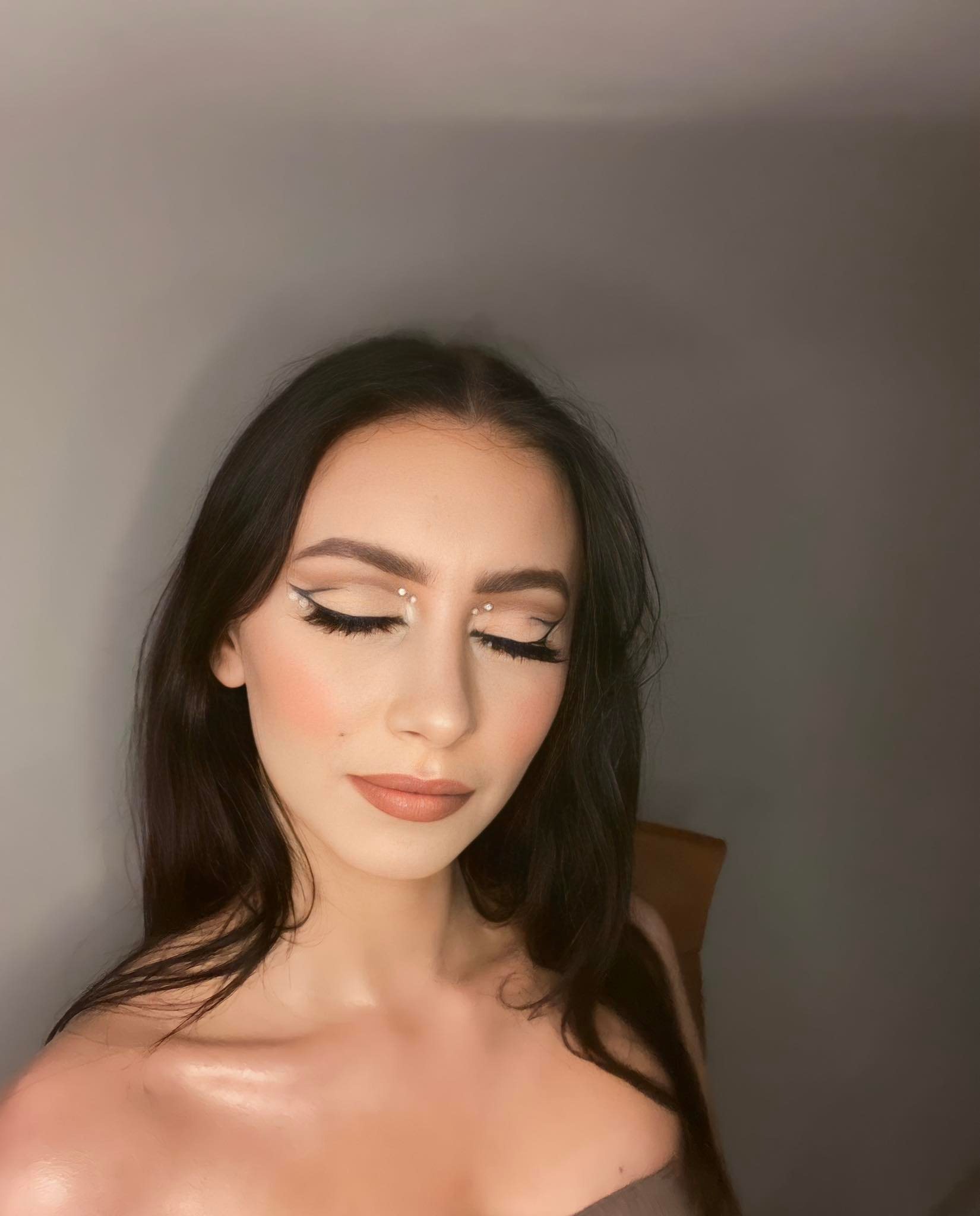 Portret kobiety z zamkniętymi oczami, prezentującej delikatny, wieczorowy make-up z białymi akcentami i sztucznymi rzęsami, na gładkim, szarym tle.