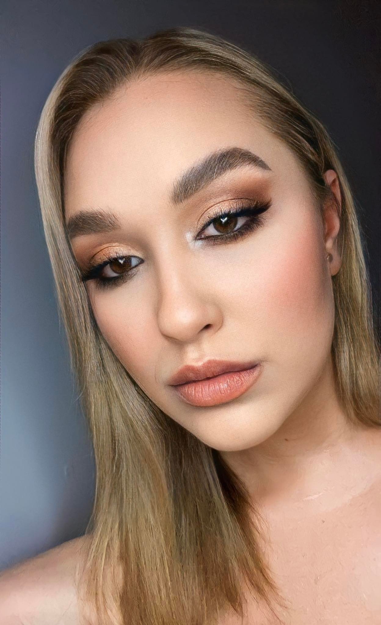 Portret kobiety z profesjonalnie wykonanym, ciepłym, brązowym cieniowaniem powiek, wyraźną czarną kreską i delikatnym konturowaniem twarzy, podkreślającym kości policzkowe.