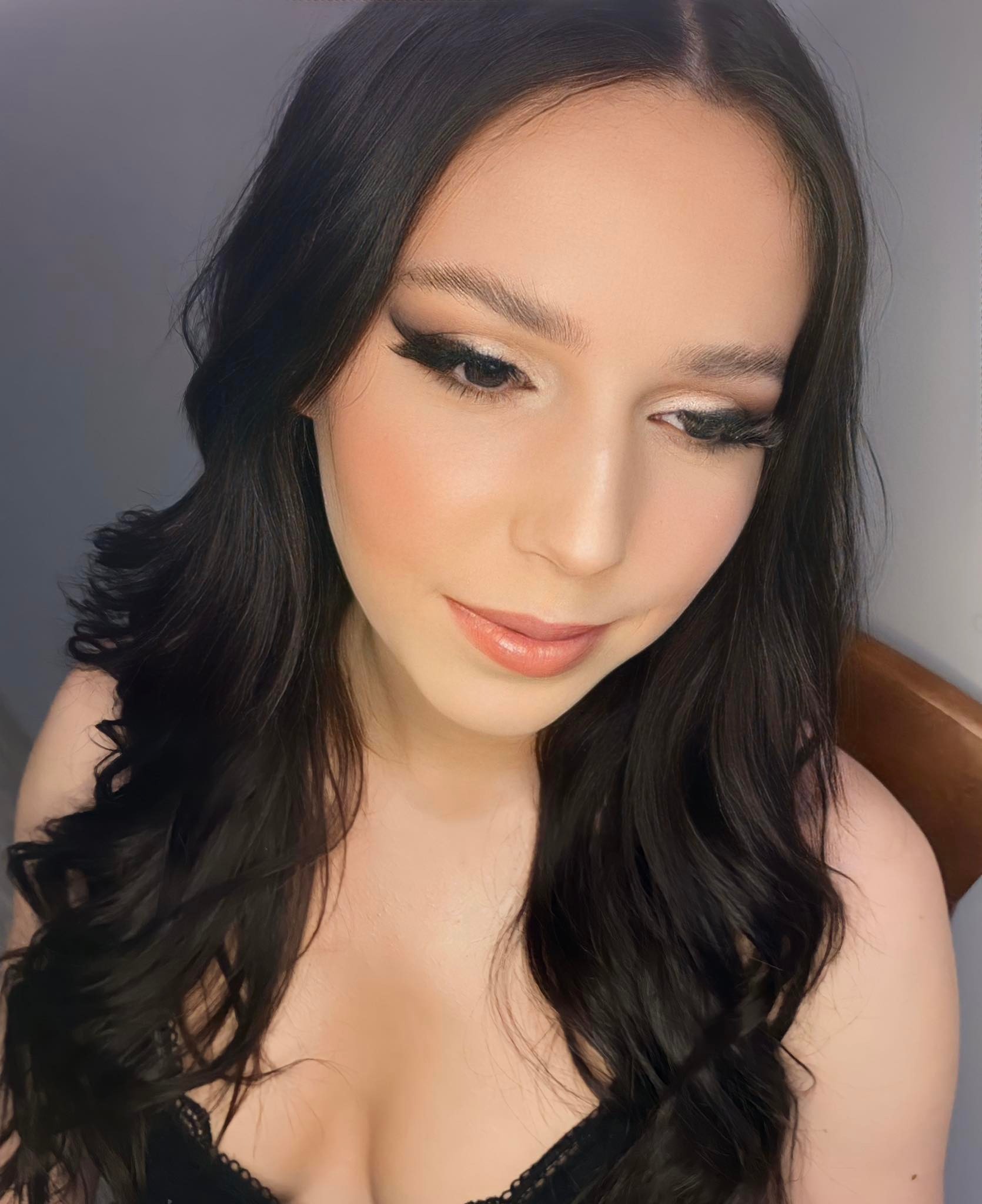 Portret kobiety z profesjonalnie wykonanym, delikatnym wizażem, z wyraźnie podkreślonymi oczami i długimi, ciemnymi włosami opadającymi falami.