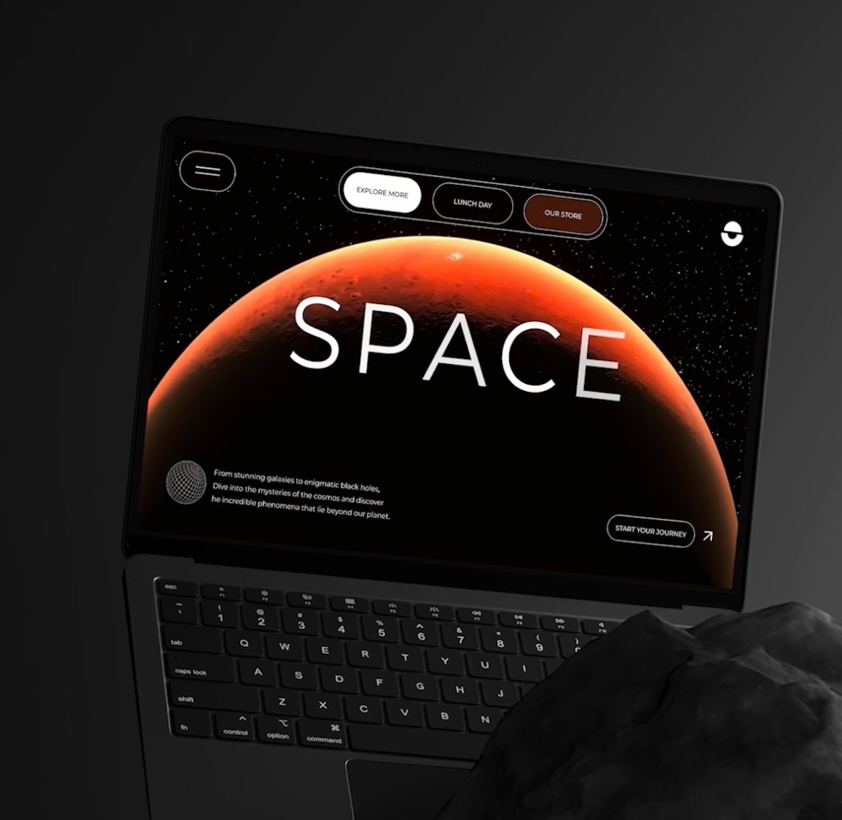 Laptop wyświetlający stronę internetową o tematyce kosmicznej z napisem 'SPACE', z widoczną dłonią na klawiaturze i ciemnoszarym tłem.