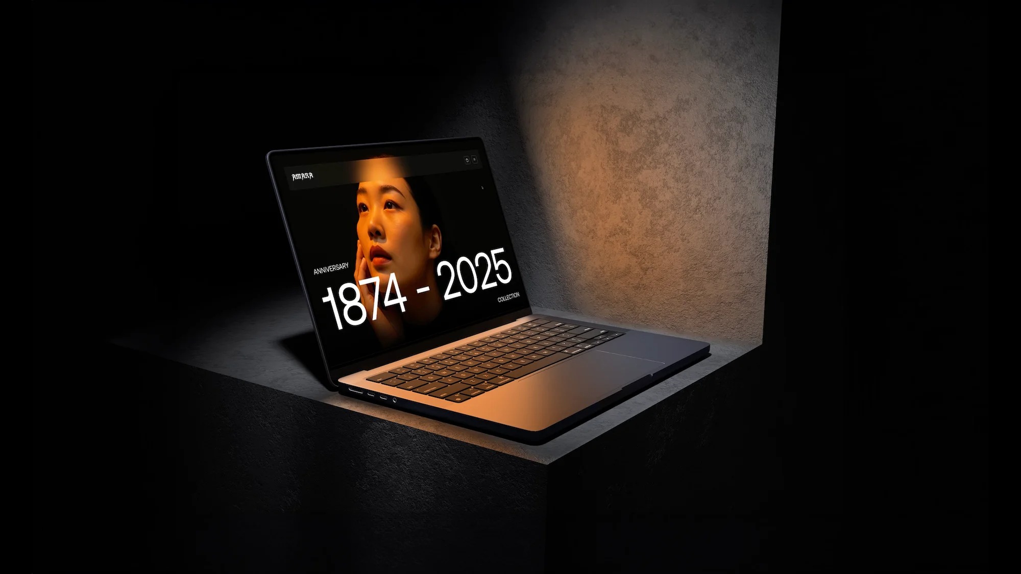 Laptop z wyświetloną stroną internetową prezentującą portret kobiety i daty 1874-2025, umieszczony na betonowej powierzchni w minimalistycznym, ciemnym otoczeniu.