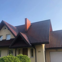 Michał Szwed G - Roof - Ciemnobrązowy dach z blachodachówki na beżowym domu z ceglanym kominem, numer domu 105, widok z dołu w słoneczny dzień.