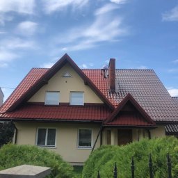 Michał Szwed G - Roof - Częściowo pomalowany dach z czerwonej dachówki, widoczny pracownik na dachu, drabina oparta o ścianę domu, błękitne niebo z chmurami w tle.