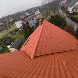 Michał Szwed G - Roof - Czerwony dach z dachówki ceramicznej, widok z góry na tle zabudowy jednorodzinnej i drzew. Dach po renowacji, z widoczną fakturą dachówki.